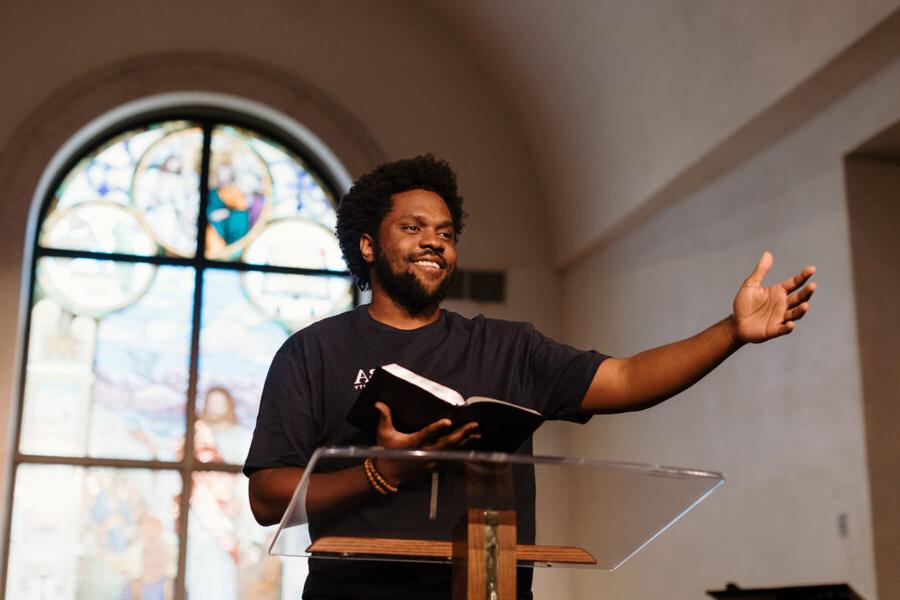 PBA student reads the bible with arm outstretched at the front of chapel.